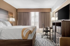 A hotel room with a bed, desk, TV, and refrigerator.