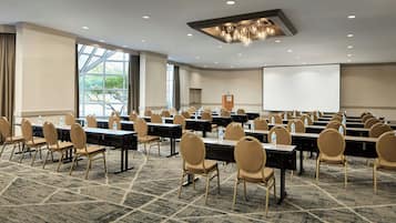 A conference room with rows of tables and chairs, a projector screen, and a large window.