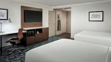A hotel room with a desk, chair, two beds, a mirror, and framed pictures on the walls.