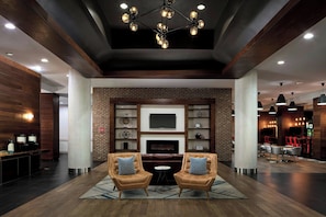 A modern lounge area with leather armchairs, a fireplace, and a brick wall with shelves. - Four Points by Sheraton Richmond (Richmond)