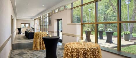 A hotel corridor with a long view of the outdoors, featuring large windows and a carpeted floor.