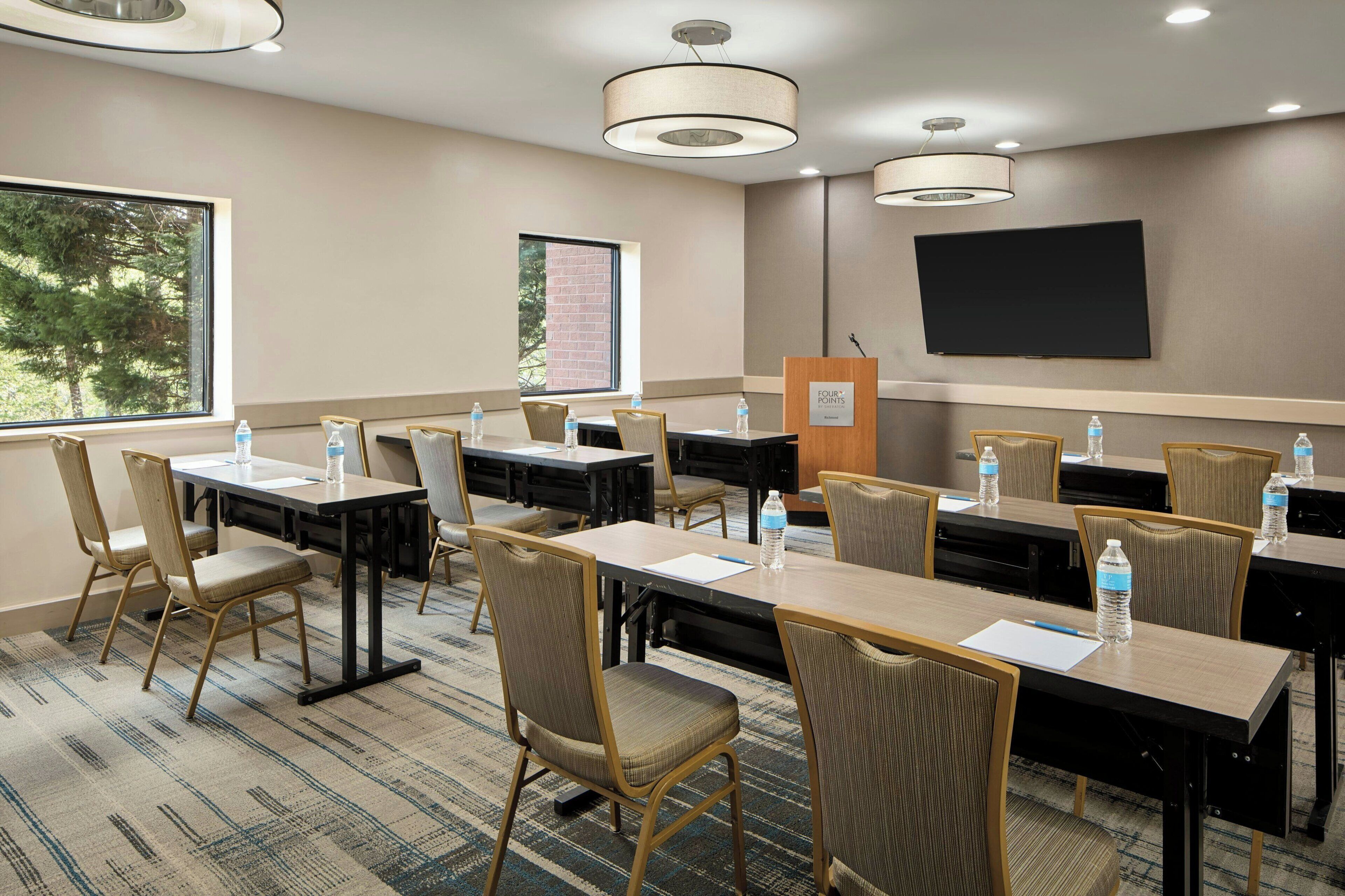 A conference room with multiple tables and chairs, a podium, and a large screen on the wall.