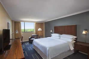 Relax in comfort with a large bed, desk, and chair, surrounded by natural light and stylish furnishings.