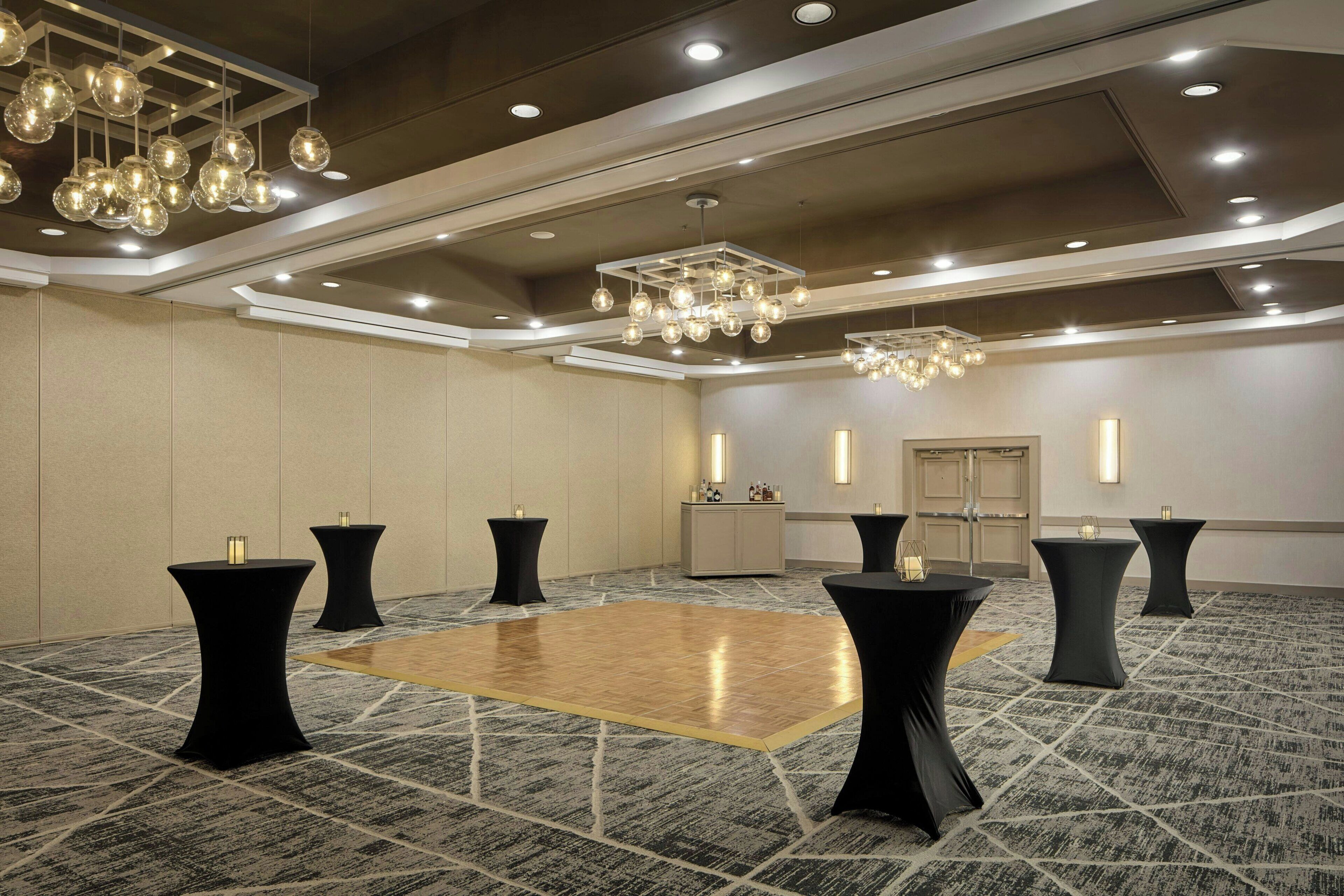 Une salle de conférence spacieuse, dotée d’un parquet en bois poli, de tables rondes noires et d’un lustre moderne.
