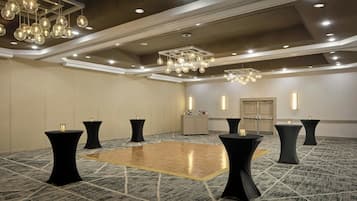 Une salle de conférence spacieuse, dotée d’un parquet en bois poli, de tables rondes noires et d’un lustre moderne.