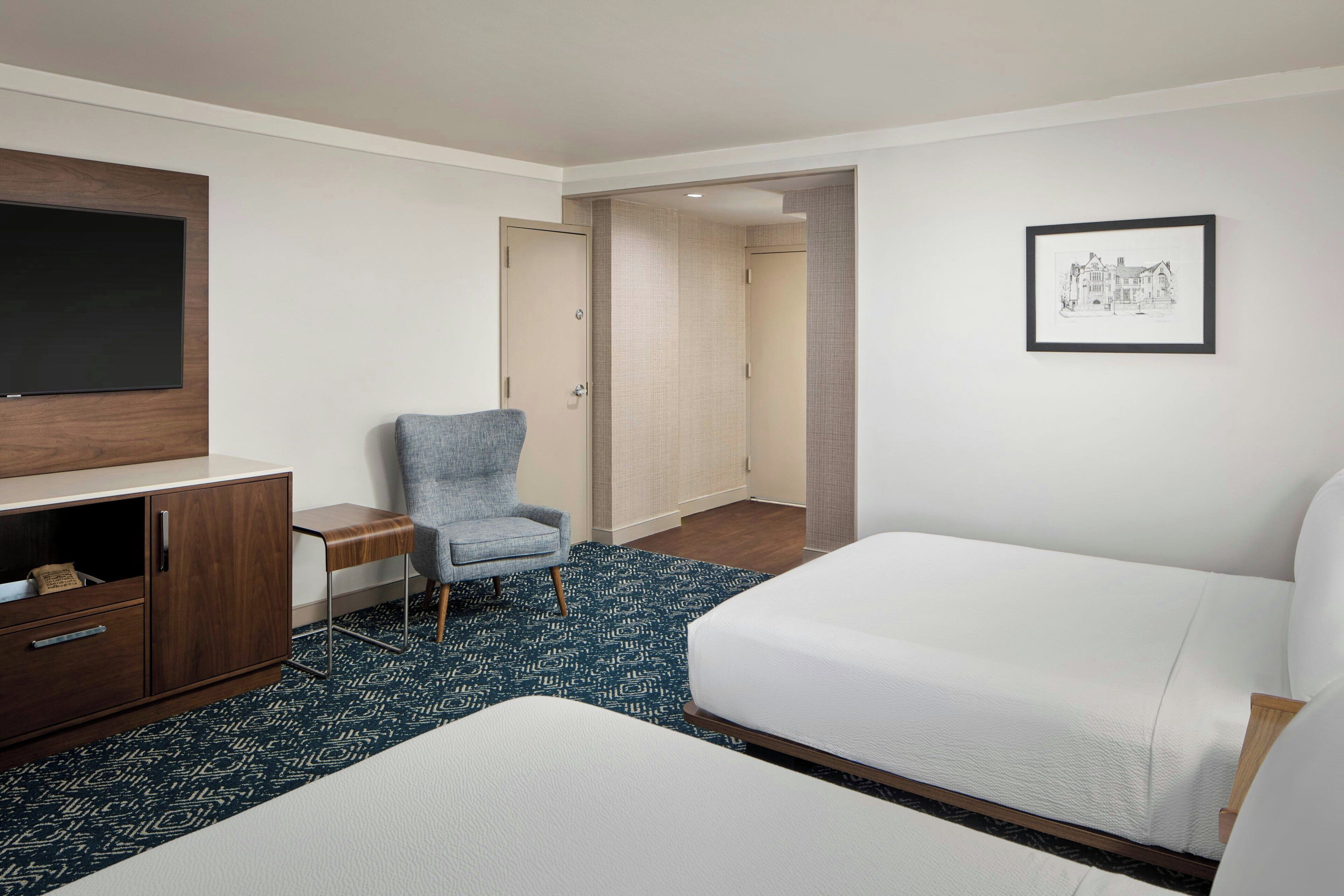 A hotel room with a bed, a desk, a chair, a television, and a framed picture on the wall.