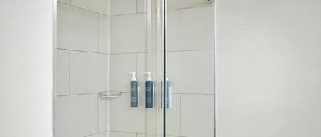 A glass-enclosed shower stall with a handrail, a tiled floor, and a sign advising to 'ASE SLIDE DR GENTLY'.