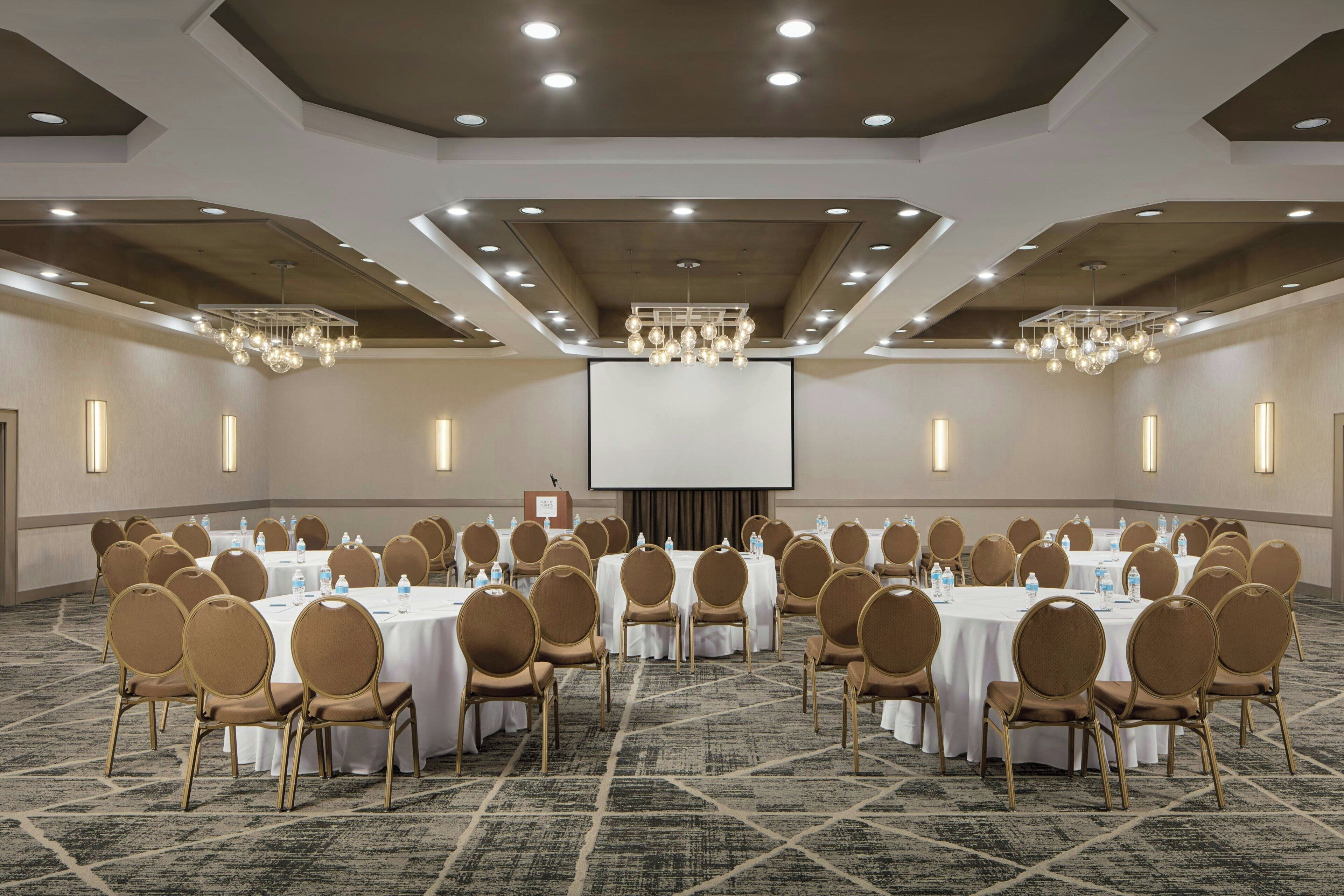 Une salle de conférence équipée de tables rondes et de chaises, d’un grand écran et d’un pupitre.