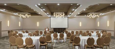 A conference room with round tables and chairs, a large screen, and a podium.