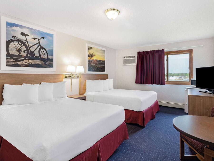 Habitación de hotel con dos camas, un escritorio, un televisor y ventana con vistas.