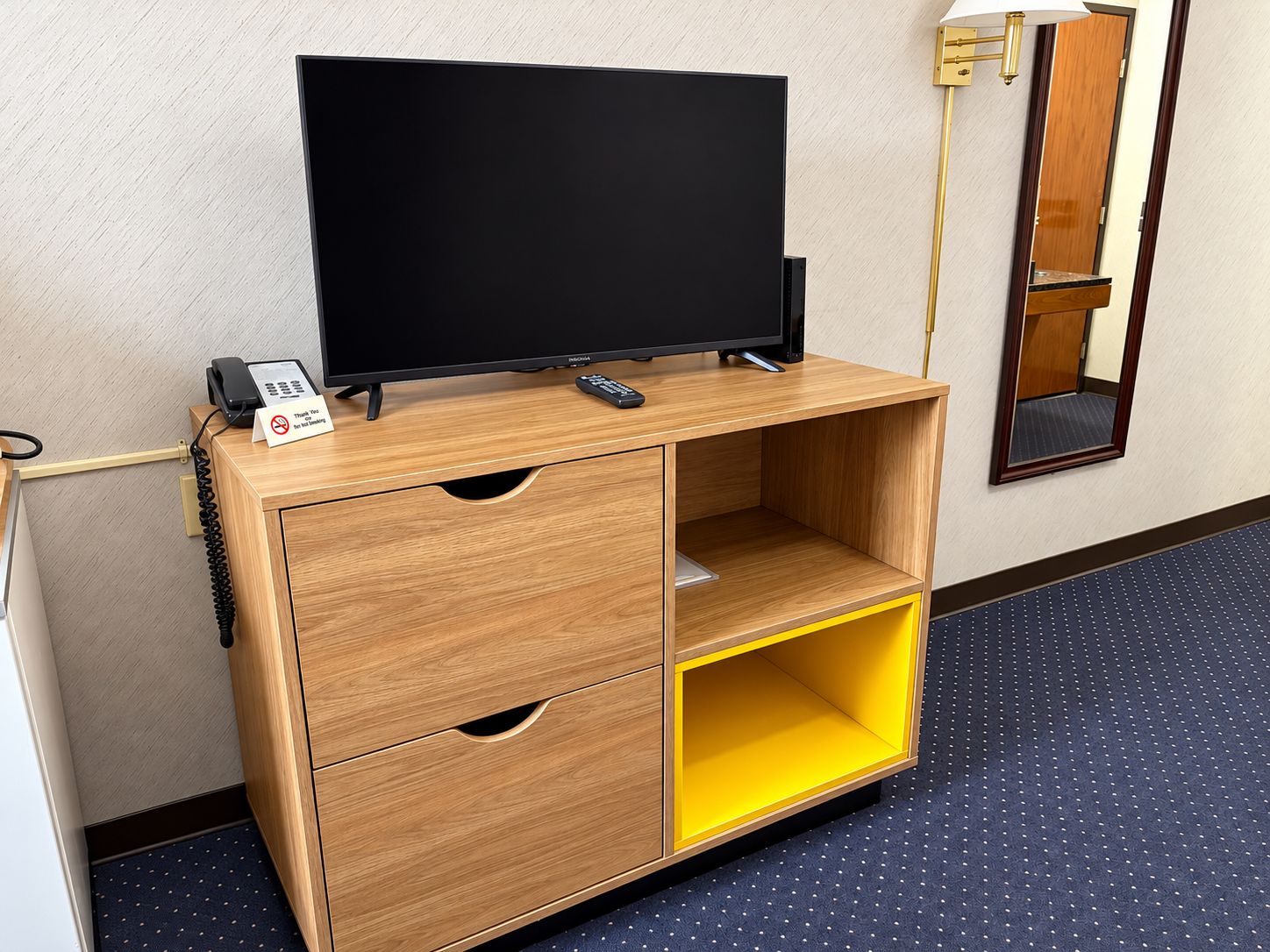 Un mobiletto in legno porta TV con televisore a schermo piatto, un telefono e un telecomando.