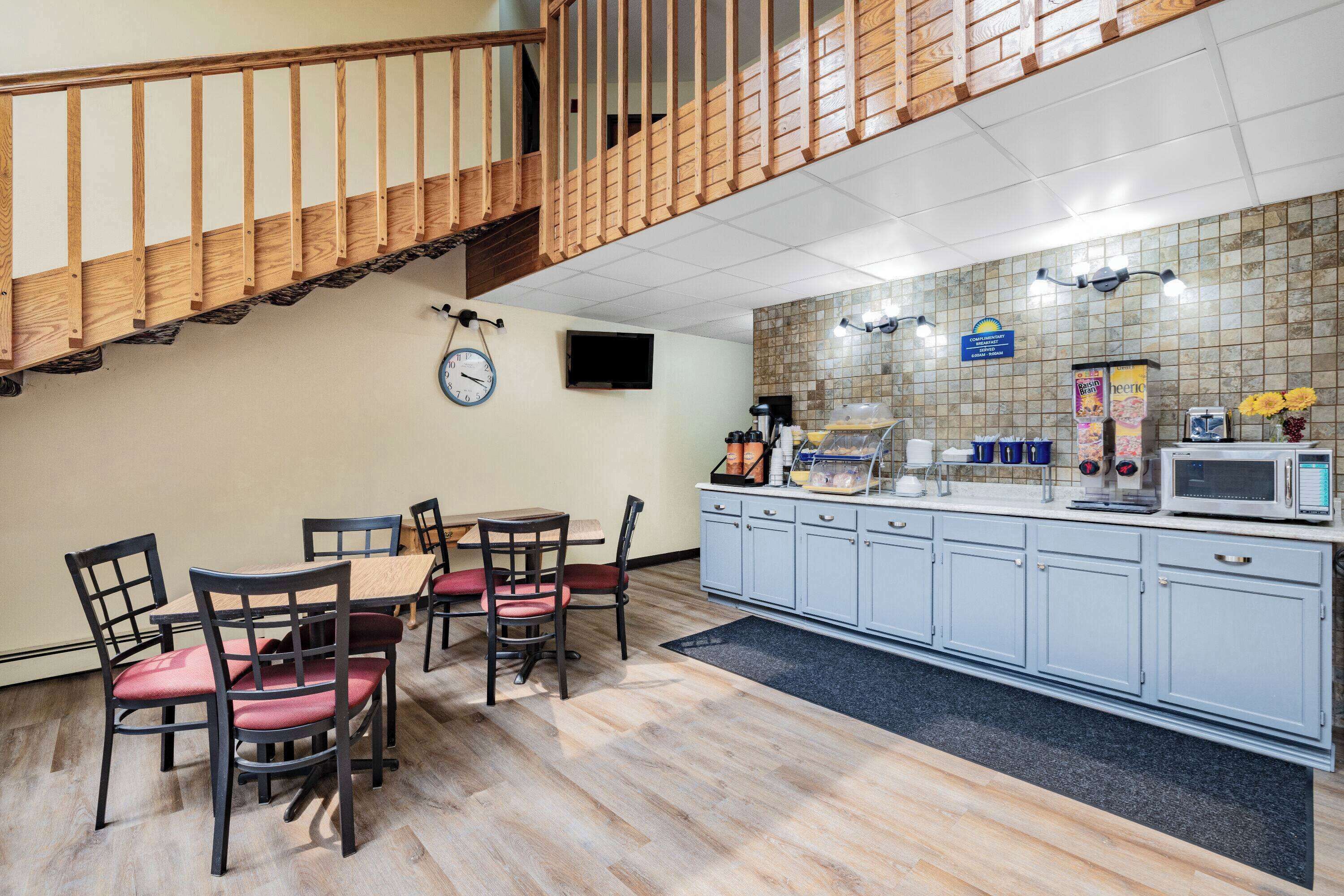 A hotel kitchen with a dining area, wooden staircase, and tiled backsplash.