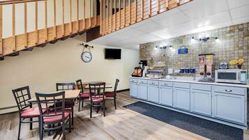 A hotel kitchen with a dining area, wooden staircase, and tiled backsplash.
