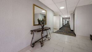 A hallway with a mirror, a console table with a vase, and a patterned carpet. - Quality Inn University Area (Farmville)