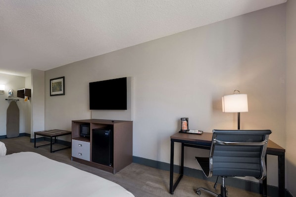 Una habitación de hotel con cama, escritorio, silla, televisor, lámpara y minibar.