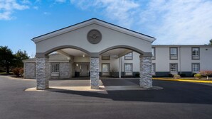 A building with a central entrance under a covered canopy, flanked by stone pillars, and a flat-roofed structure to the right. - Quality Inn University Area (Farmville)
