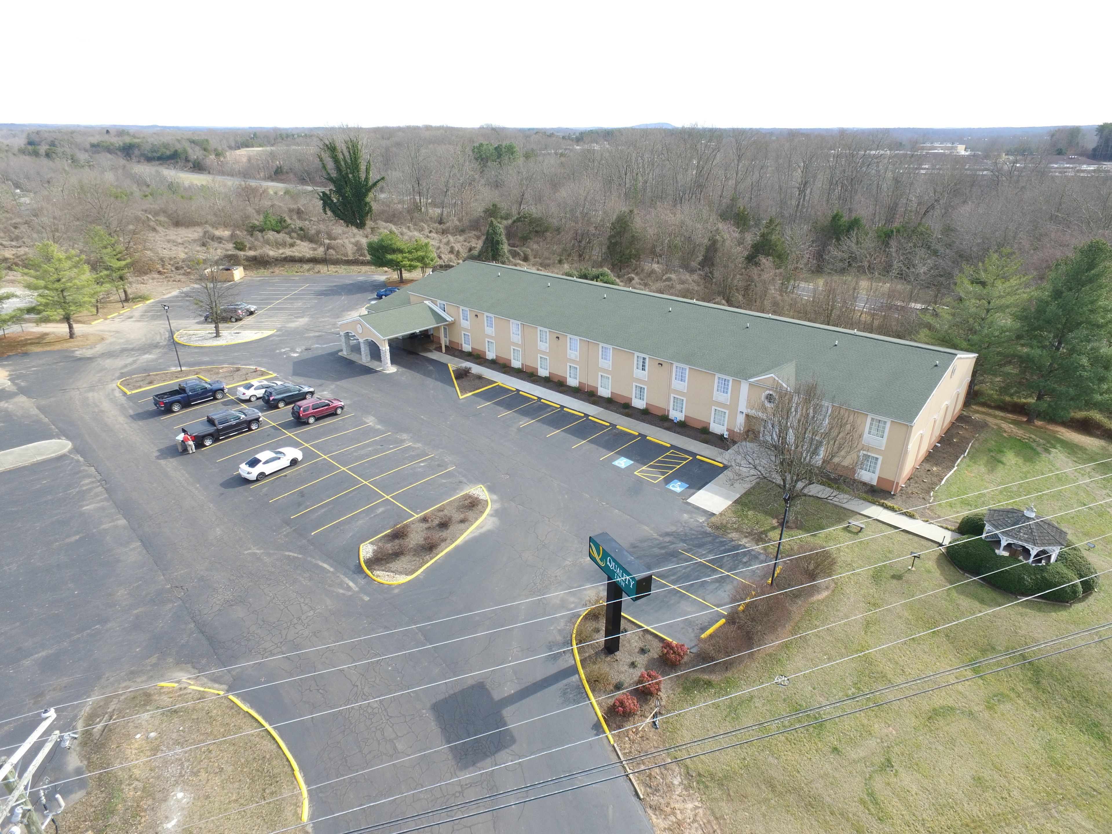 An aerial view of a hotel with a parking lot, a green-roofed building, and a landscaped area with trees and shrubs.