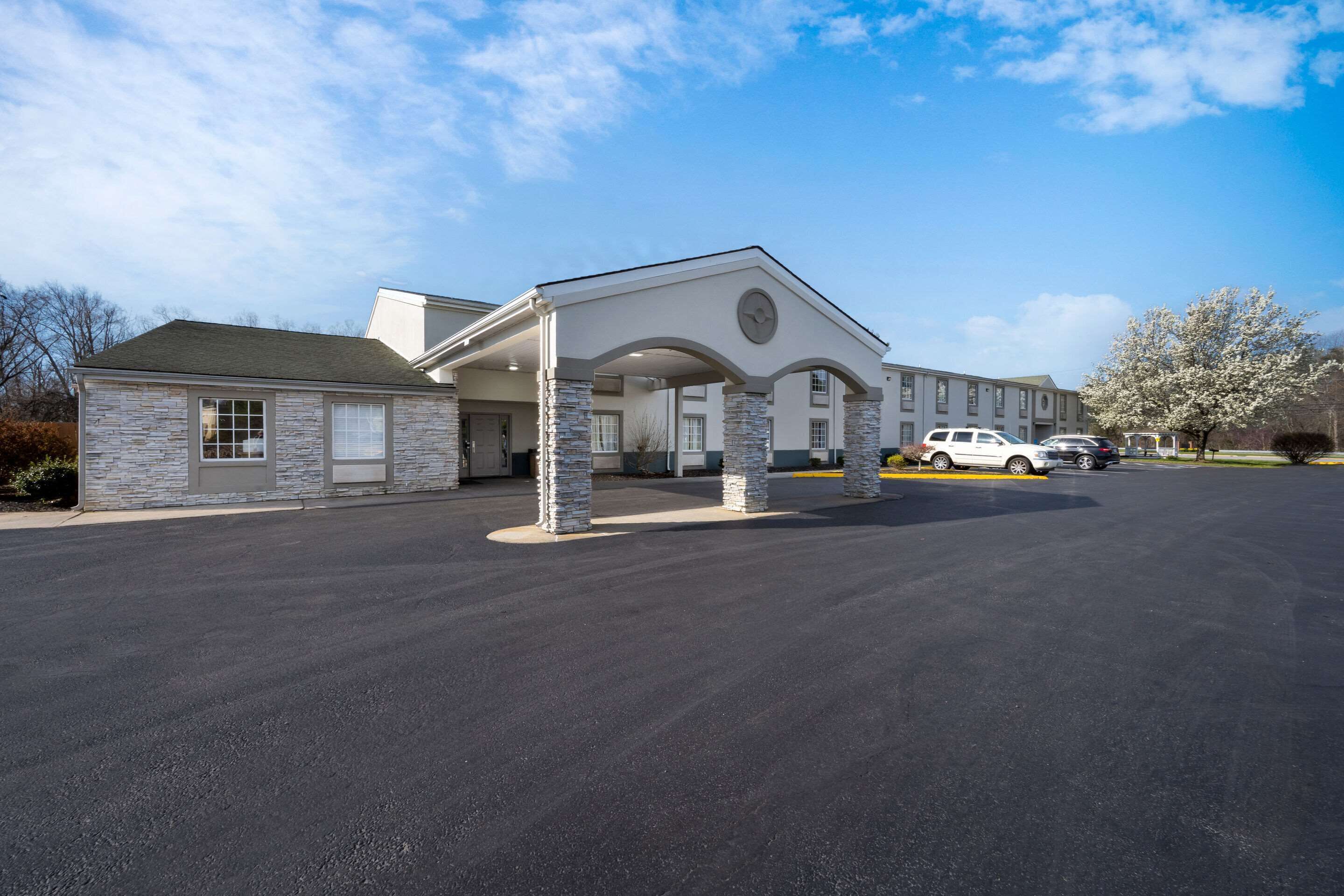 A hotel with a stone facade, a covered entrance, and a parking lot with several cars.