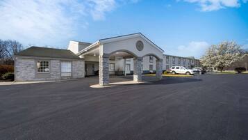 A hotel with a stone facade, a covered entrance, and a parking lot with several cars.