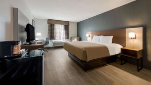 A hotel room with a bed, bedside tables, a desk with a computer, a television, and a window with curtains. - Quality Inn University Area (Farmville)