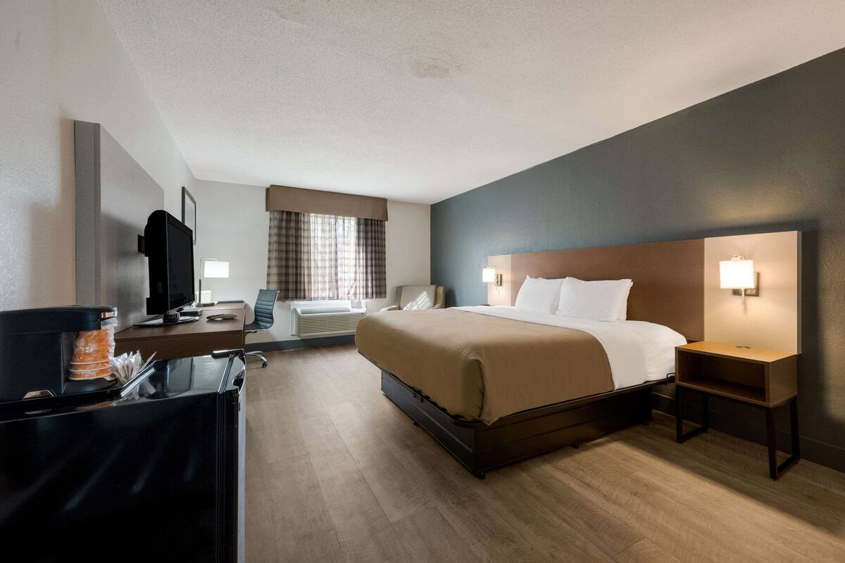 A hotel room with a bed, bedside tables, a desk with a computer, a television, and a window with curtains.