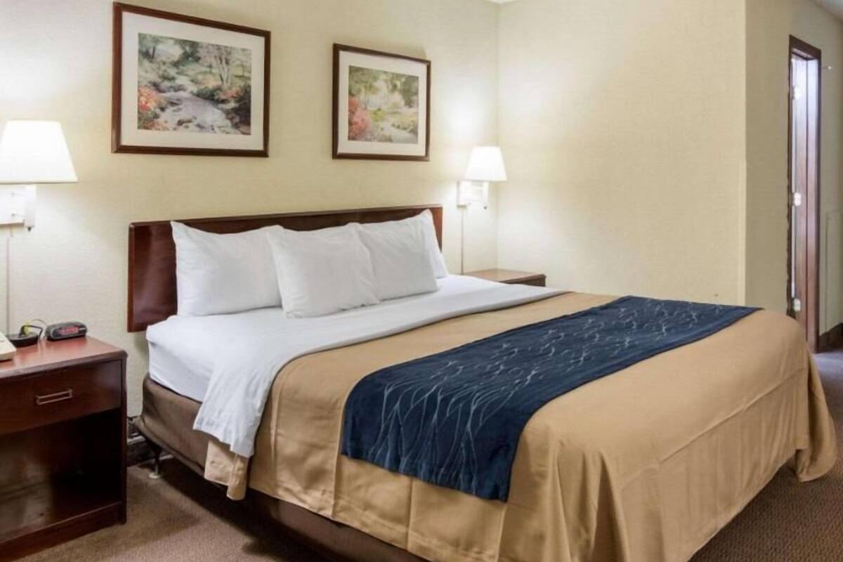 A hotel room with a bed, two wall-mounted lamps, and two framed pictures on the wall.