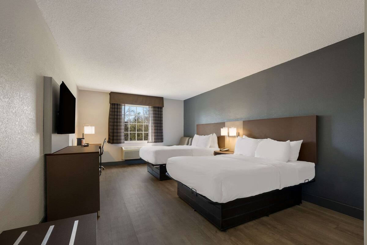 A hotel room with two beds, a desk, a TV, and a window with curtains.