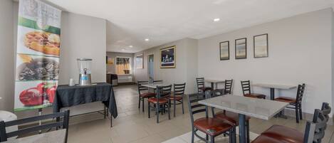 A modern dining area with tables and chairs, a banner advertising breakfast, and framed pictures on the wall.