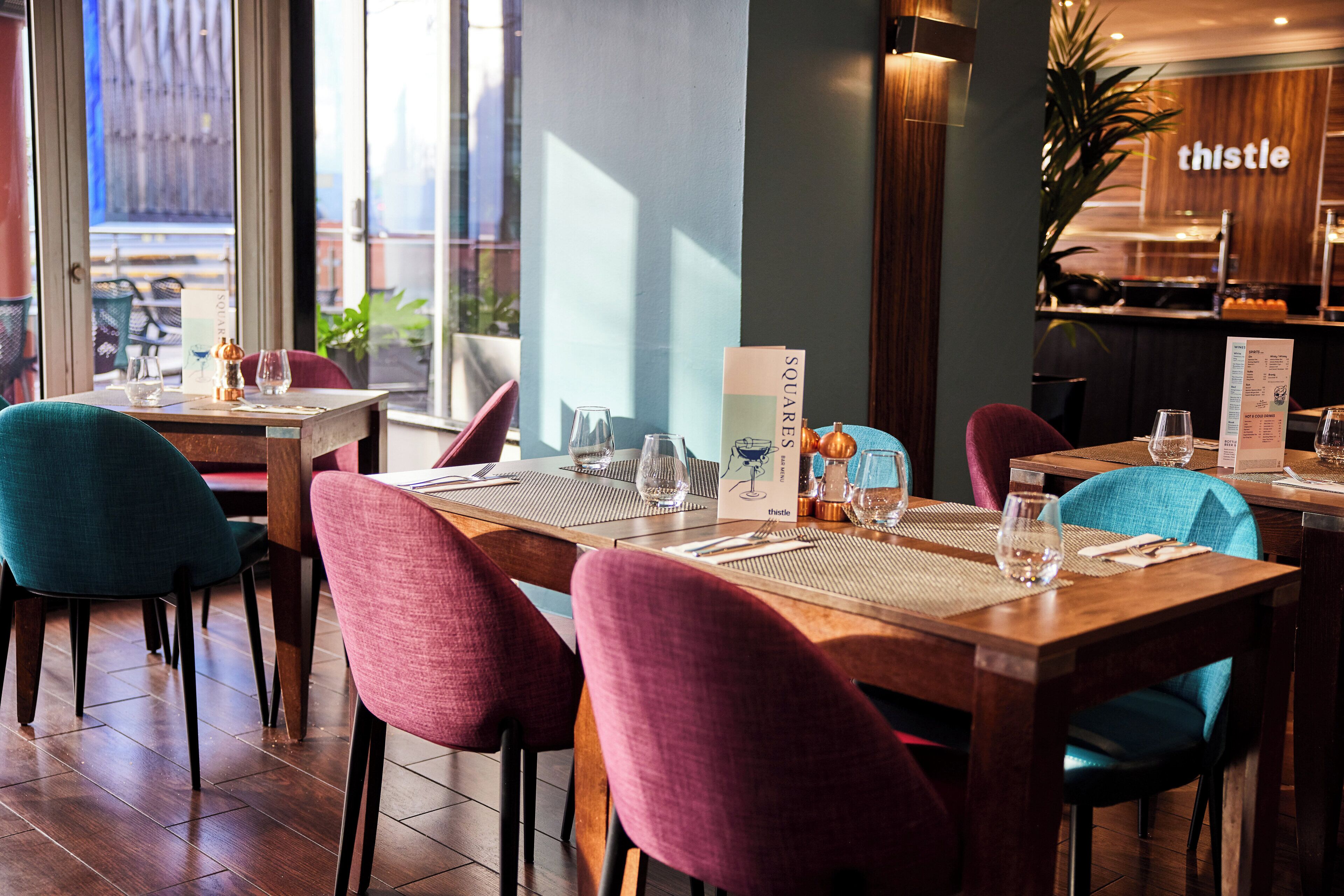 A restaurant interior with wooden tables, colorful chairs, and a menu stand.