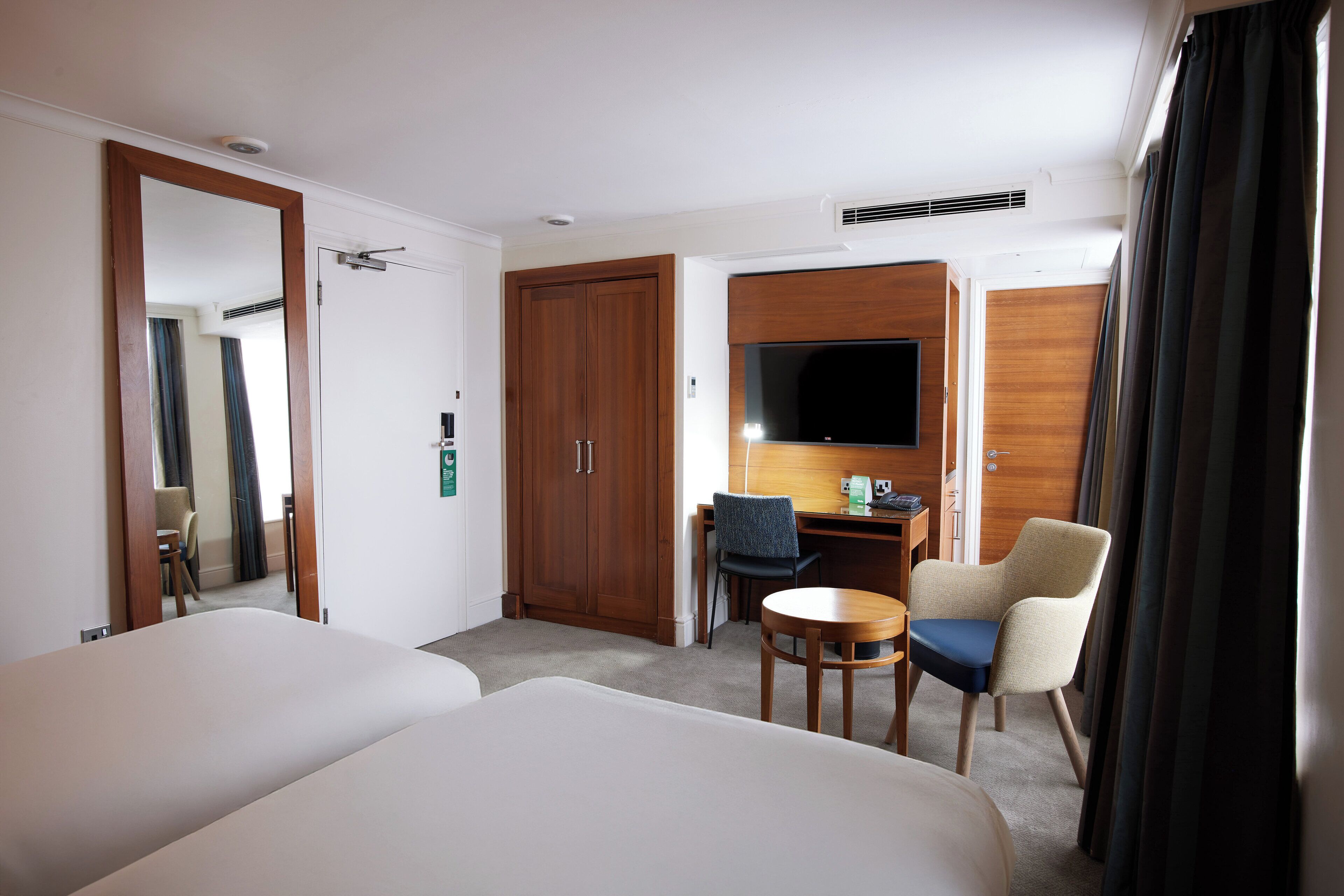 A hotel room with two beds, a desk, a chair, a TV, and a wardrobe.