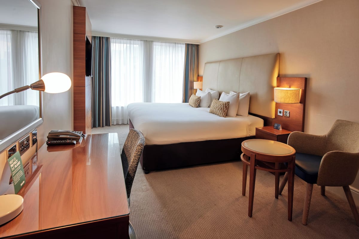 Ett hotellrum med en säng, ett skrivbord, en stol, en lampa och en tv.