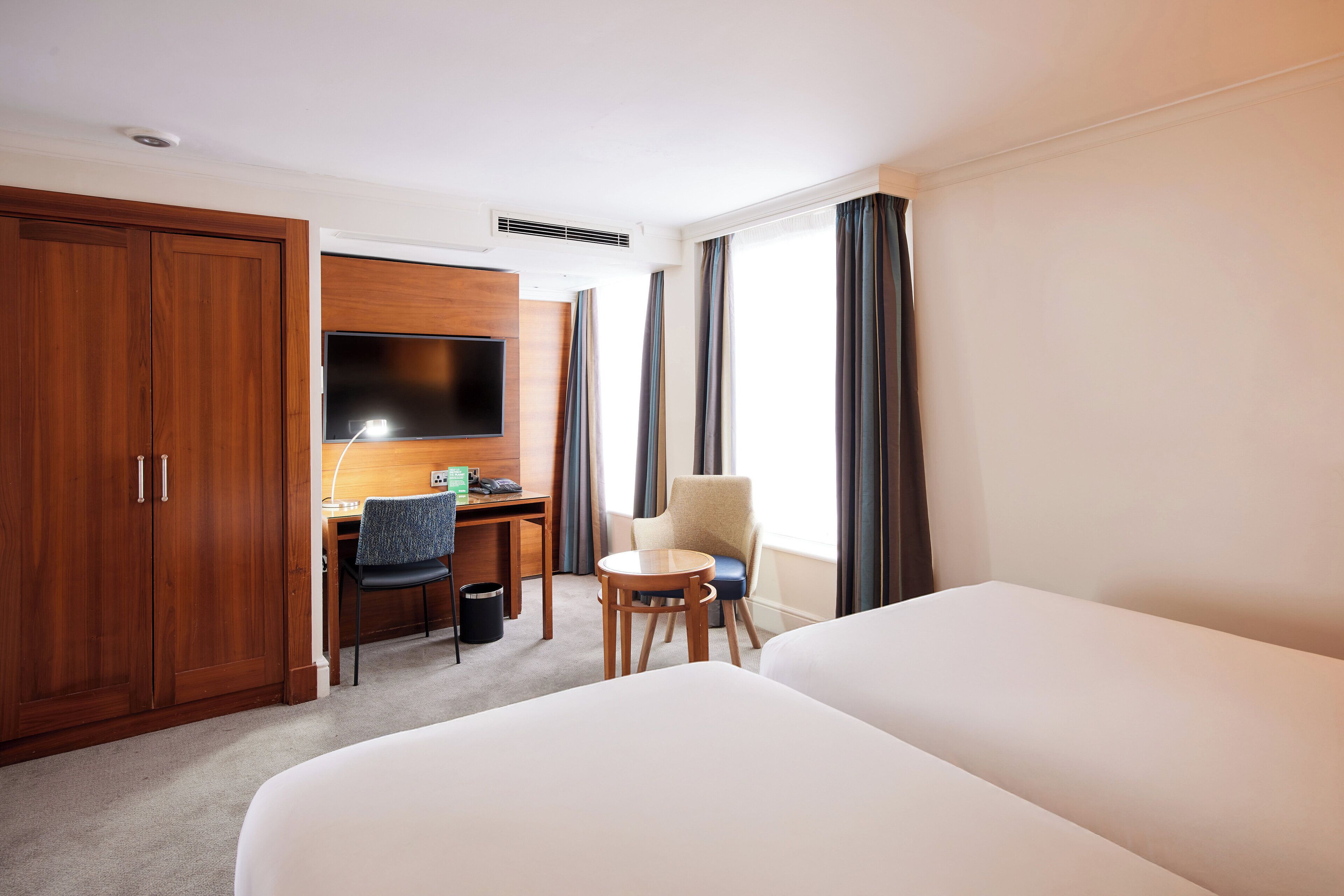 A hotel room with a bed, a desk with a chair, a TV, and a wardrobe.
