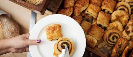 A variety of pastries on display, including croissants and rolls, with a person holding a plate with a pastry.