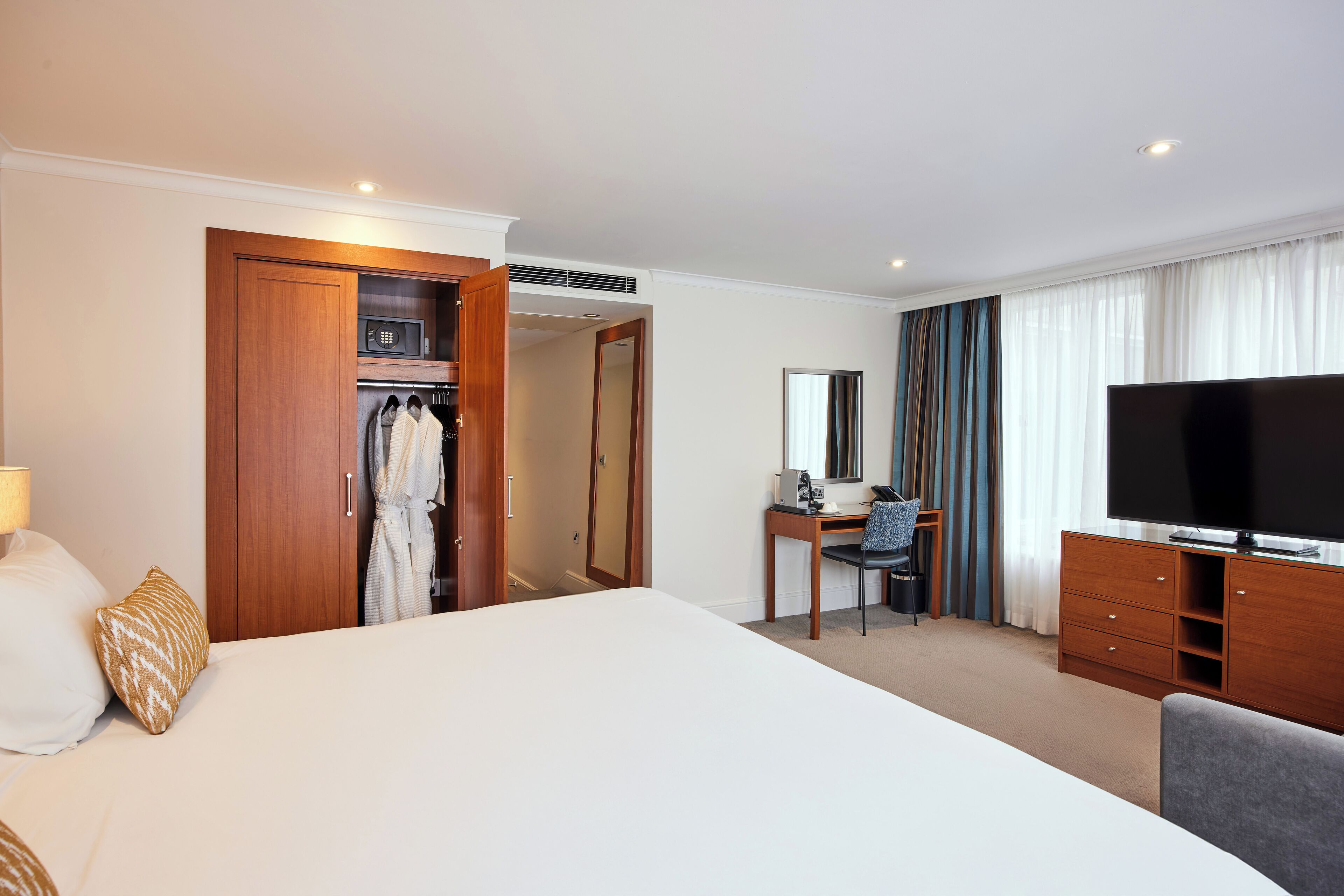 A hotel room with a large bed, a desk with a chair, a television, and a wardrobe.