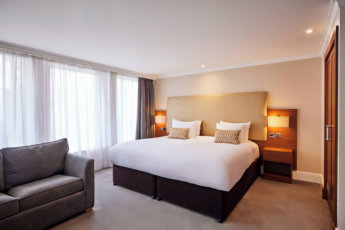 Ett hotellrum med en stor säng, en soffa, två sänglampor och ett fönster med gardiner.