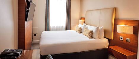 Een hotelkamer met een groot bed, bedlampjes, een flatscreen televisie aan de muur en een bureau met telefoon.