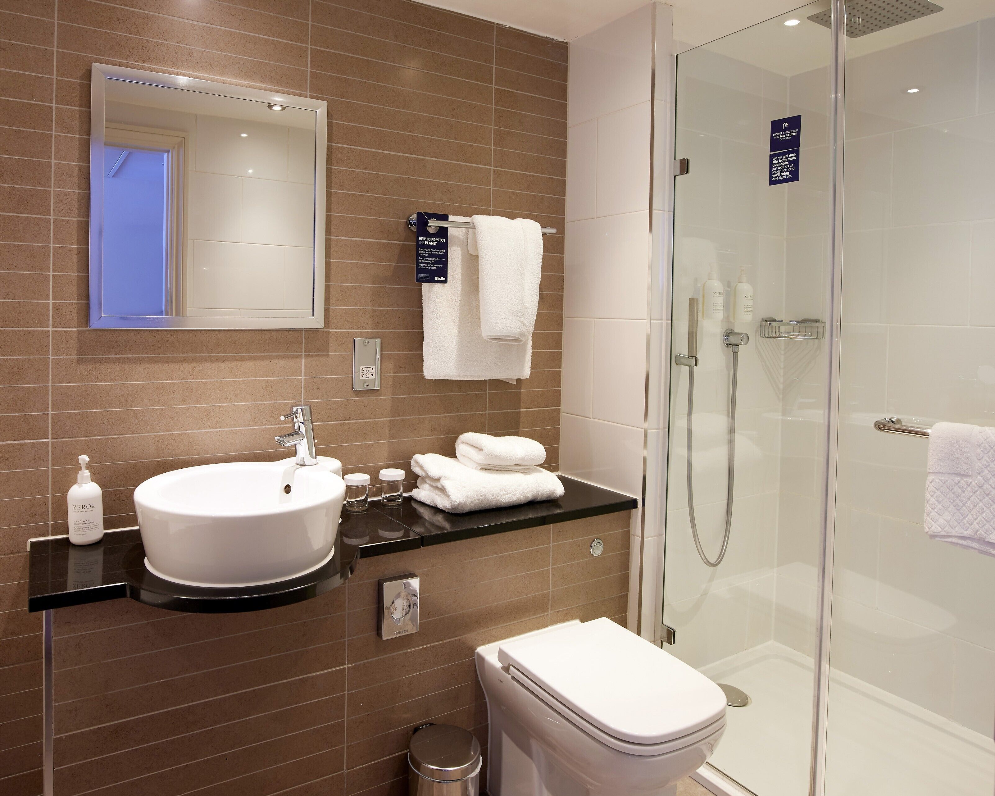 Un baño moderno con lavamanos, espejo y ducha con mampara de vidrio.