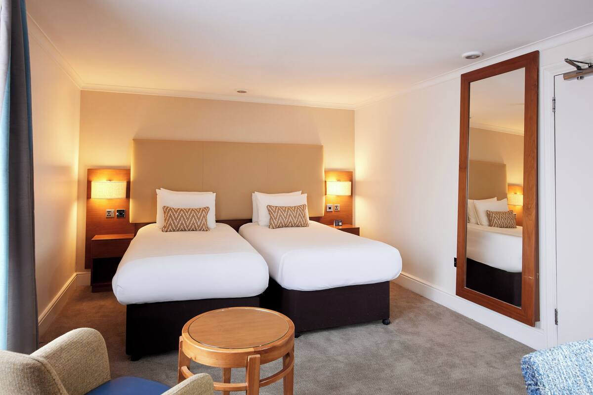 Ett hotellrum med två sängar, sänglampor, ett runt träbord och en stor spegel.