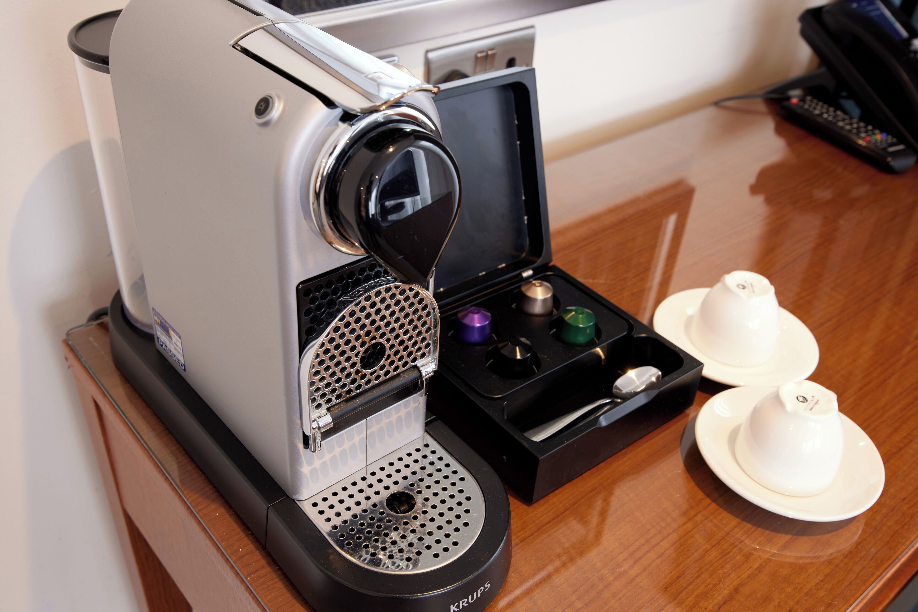Une machine à café, avec un présentoir à tasses et une télécommande, posée sur une table en bois.