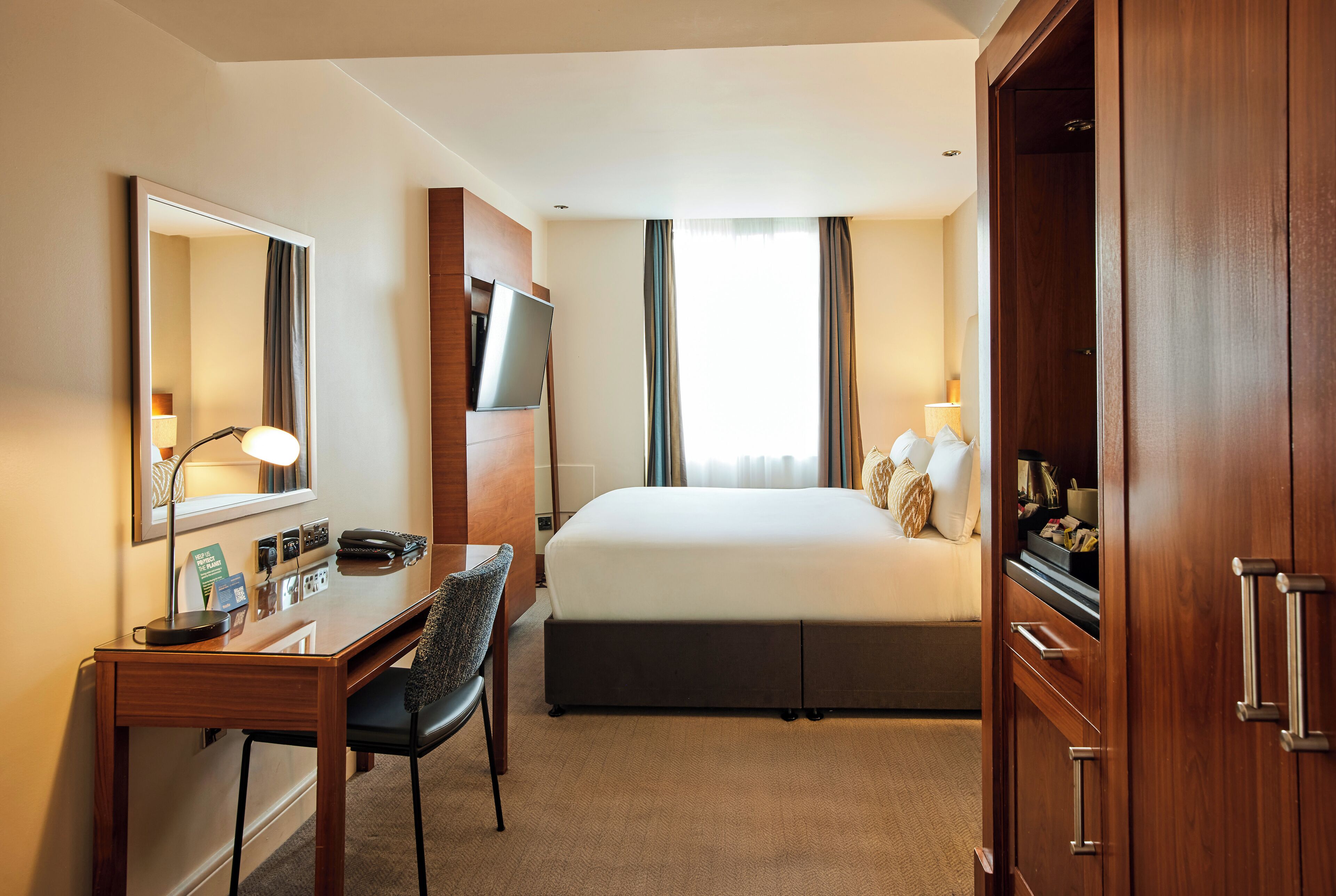 A hotel room with a bed, desk, chair, and wardrobe.