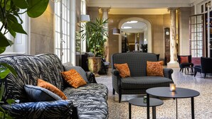 A spacious lobby with a patterned sofa, armchairs, and a small table. - Hôtel Oceania Le Métropole Montpellier (Montpellier)
