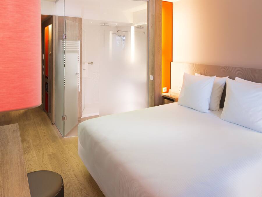 Habitación de hotel con una cama grande, un escritorio de madera y una puerta de vidrio que da a un área de ducha.