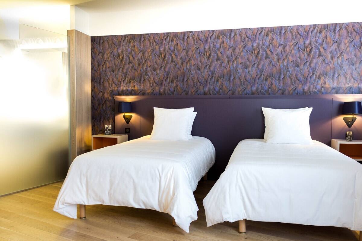 Een hotelkamer met twee éénpersoonsbedden, een gestructureerde wand en bedlampjes.