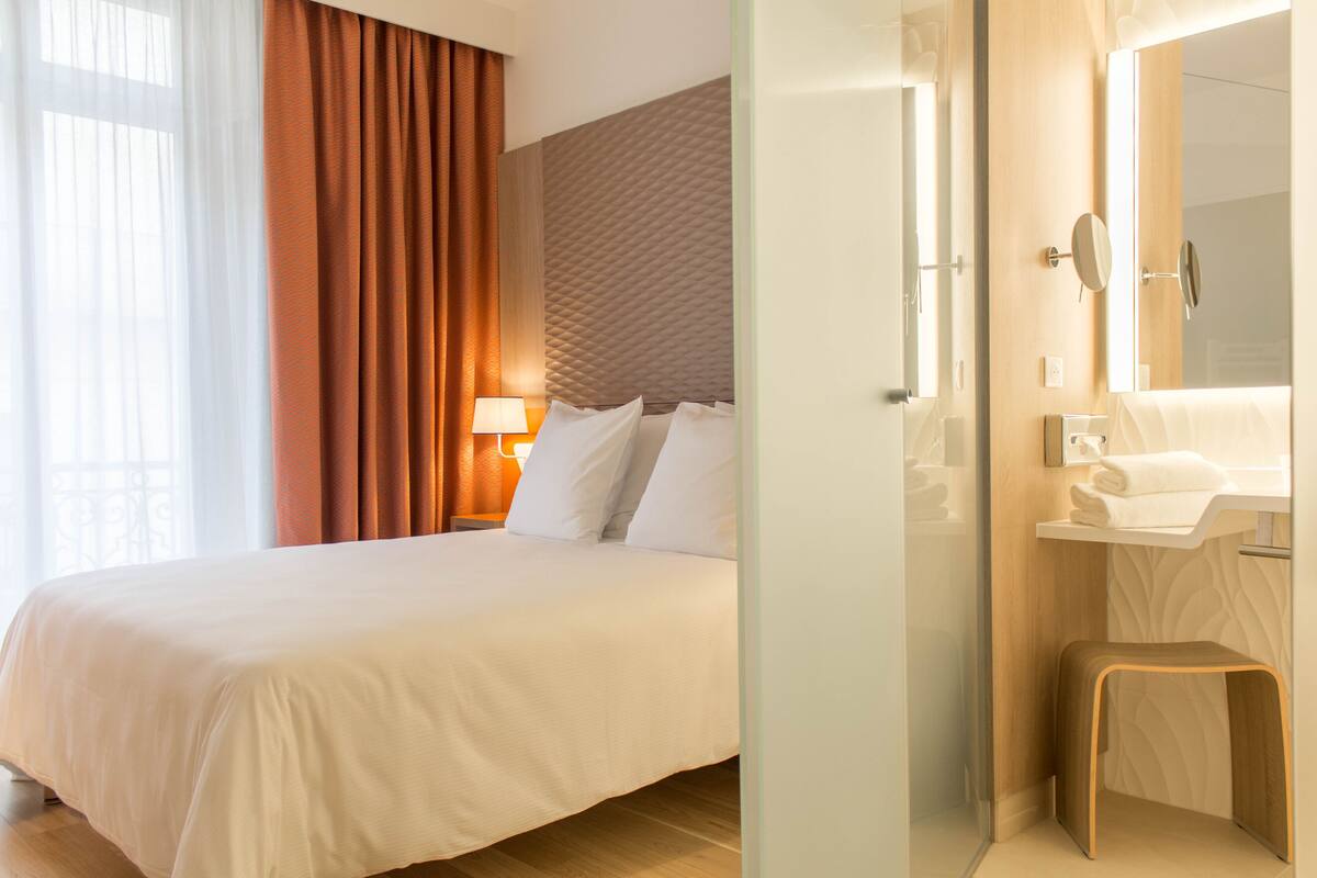 Een hotelkamer met een groot bed, een bedlamp, een spiegel en een klein krukje.