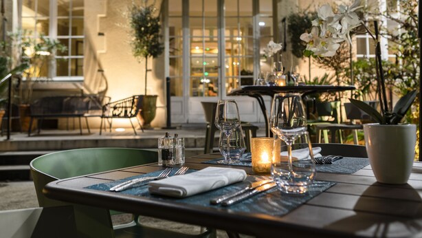 An outdoor dining area with tables set for two, featuring a candle centerpiece, clear glasses, and neatly arranged cutlery. - Hôtel Oceania Le Métropole Montpellier (Montpellier)