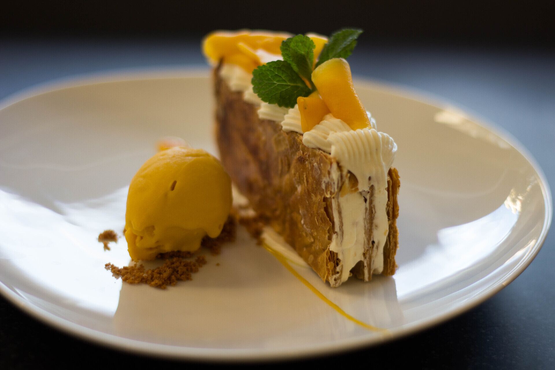 Un dessert servi sur une assiette blanche, composé d’une part de gâteau recouverte de crème et de fruits, et d’une boule de glace à côté.