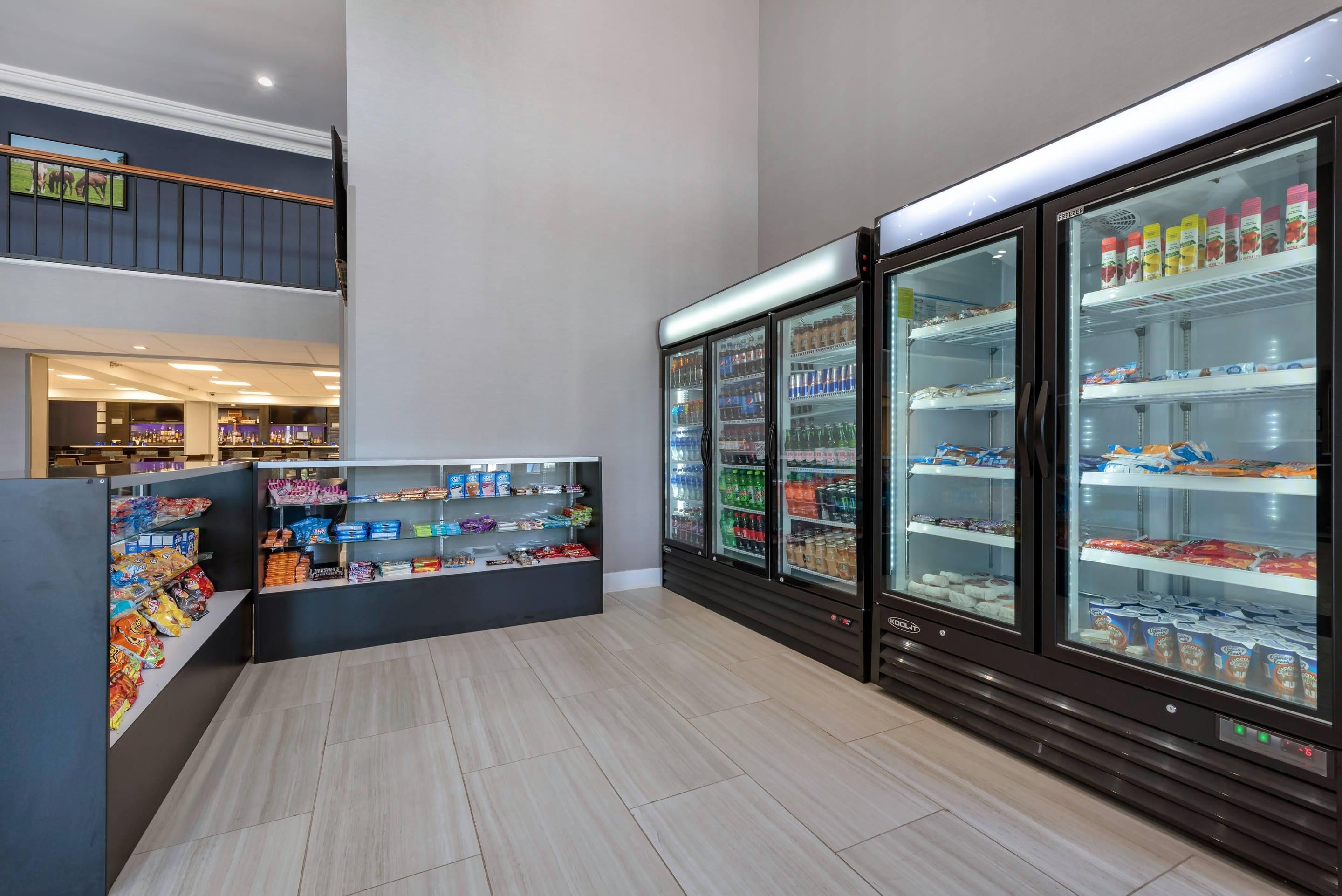 Un espacio interior limpio y bien iluminado con una barra de aperitivos, vitrinas refrigeradas y una escalera que sube a un nivel superior.