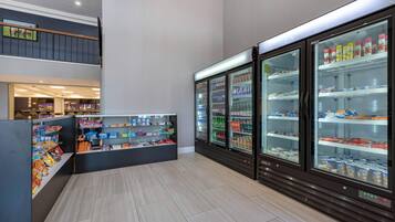 Un espacio interior limpio y bien iluminado con una barra de aperitivos, vitrinas refrigeradas y una escalera que sube a un nivel superior.