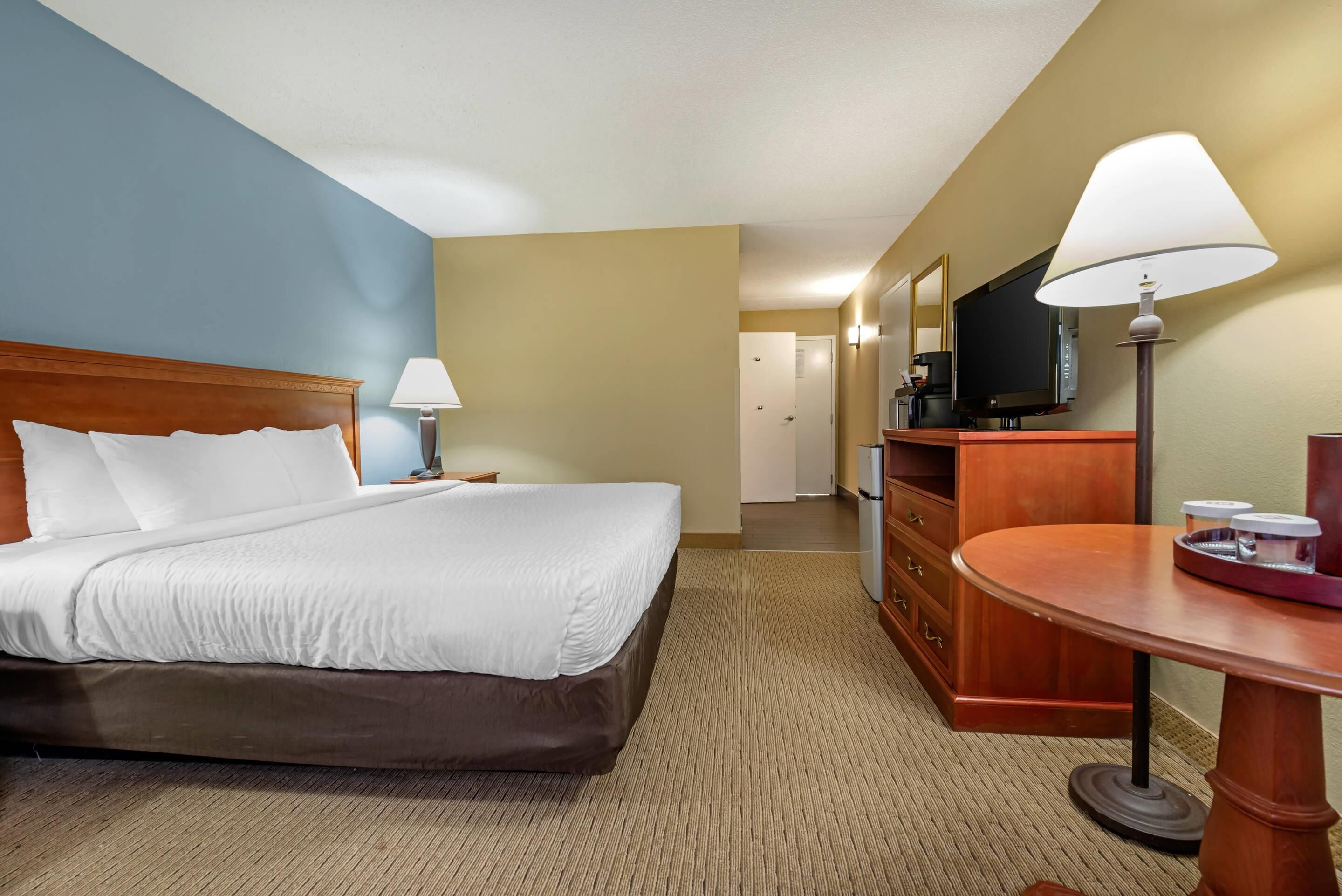 A hotel room with a bed, a desk, a chair, a lamp, a television, and a dresser.