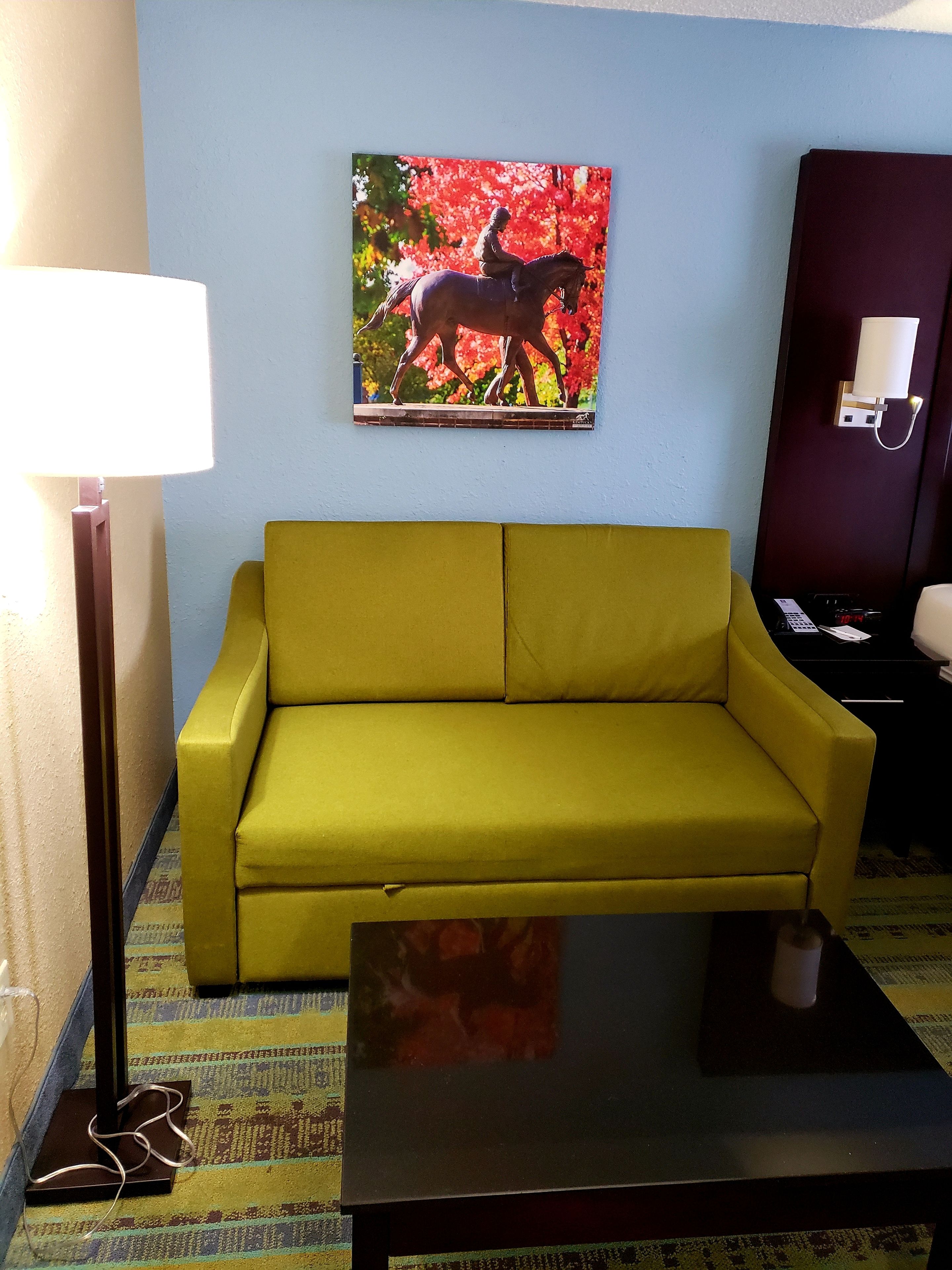 A yellow sofa, a small table, a lamp, and a painting of a horse.